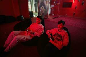 Father and son play gamepad video game console in red gaming room. Dad and kid gamers. photo