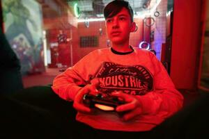 adolescente chico jugador jugar gamepad vídeo juego consola en rojo juego de azar habitación. foto