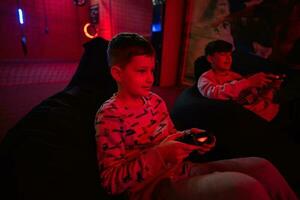 Two boys gamers play gamepad video game console in red gaming room. photo