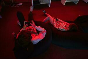 Two boys gamers play gamepad video game console in red gaming room. photo