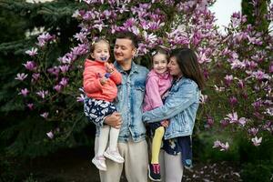 Happy family with two daughters enjoying nice spring day near magnolia blooming tree. photo