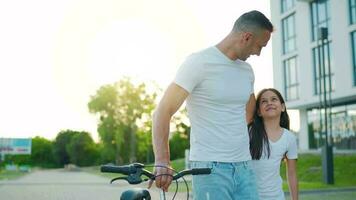 Dad is teaching daughter how to ride bicycle at sunset. Slow motion video