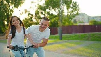 Dad is teaching daughter how to ride bicycle at sunset. Slow motion video