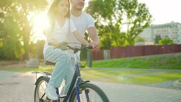 papá es enseñando hija cómo a paseo bicicleta a puesta de sol. lento movimiento video