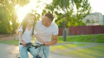 Dad is teaching daughter how to ride bicycle at sunset. Slow motion video