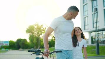 papá es enseñando hija cómo a paseo bicicleta a puesta de sol. lento movimiento video