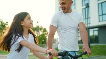 papá es enseñando hija cómo a paseo bicicleta a puesta de sol. lento movimiento video