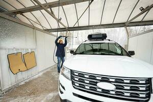 Man washing high pressure water american SUV car with roof rack at self service wash in cold weather. photo