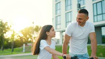 Dad is teaching daughter how to ride bicycle at sunset. Slow motion video