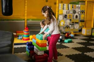 Two sisters playing at kids play center while build with colored plastic blocks. photo