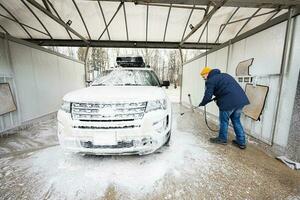 Man washing high pressure water american SUV car with roof rack at self service wash in cold weather. photo