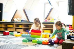 Two sisters playing at kids play center while build with colored plastic blocks. photo