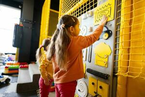 Two sisters playing with busy board at kids play center. photo