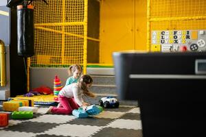 Two sisters playing at kids play center while build with colored plastic blocks. photo