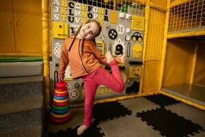 linda sonriente preescolar niña jugando con un de colores pirámide en manos en contra ocupado tablero a niños jugar centro. foto