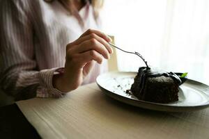 cerca arriba mano mujer sentar en café tienda café restaurante adentro y comer chocolate duende postre pastel. foto