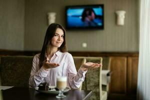 Young beautiful brunette woman sit in coffee shop cafe restaurant indoors points her hands to the side. photo