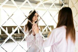 Young beautiful brunette woman in shirt touching mirror made of rhombuses. photo