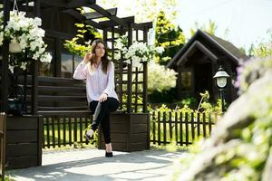 Young beautiful brunette woman in shirt sit on wooden bench with flowers in garden. photo