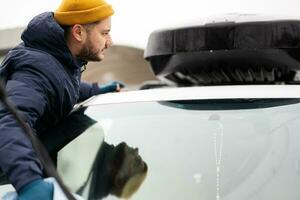 Man wipes american SUV car roof rack with a microfiber cloth after washing in cold weather. photo