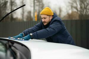 Man wipes american SUV car hood with a microfiber cloth after washing in cold weather. photo