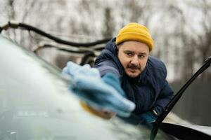 Man wipes american SUV car windshield with a microfiber cloth after washing in cold weather. photo