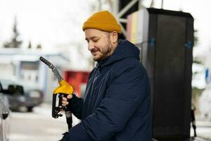 el hombre sostiene la bomba de combustible mientras reabastece su camión en la gasolinera cuando hace frío. foto