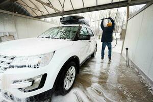 Man washing high pressure water american SUV car with roof rack at self service wash in cold weather. photo