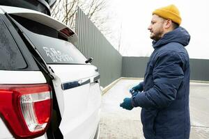 Man wipes trunk of american SUV car with a microfiber cloth after washing in cold weather. photo