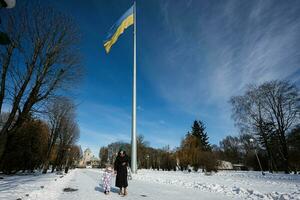 madre y niño caminando en un soleado escarchado invierno día en el parque, en contra antecedentes de un asta de bandera con el ucranio bandera. foto