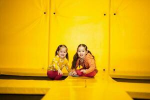 hermanos en trampolín a amarillo patio de recreo parque. hermanas durante activo entretenimientos foto