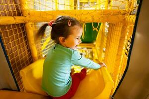 Baby girl kid slide at yellow playground park. Child in active entertaiments. photo