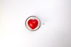 transparent glass coffee tea cup saucer with three dimension 3d red hart symbol inside on white background copy text space top view photo
