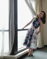 Beautiful young woman wearing modern cheongsam inspired dress standing posing next to window light photo