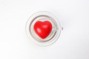 transparent glass coffee tea cup saucer with three dimension 3d red hart symbol inside on white background copy text space top view photo
