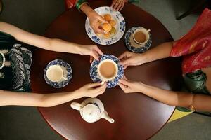 Top view of tea drink party woman hands pouring sharing teapot teacup saucer traditional biscuit Asian dress photo