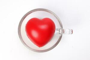 transparent glass coffee tea cup saucer with three dimension 3d red hart symbol inside on white background copy text space top view photo