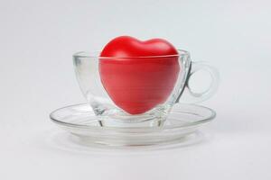transparent glass coffee tea cup saucer with three dimension 3d red hart symbol inside on white background copy text space photo