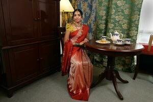 hermosa joven mujer vistiendo indio sari vestir posando hogar retro Clásico mesa ajuste foto