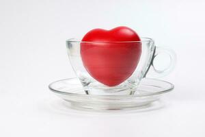 transparent glass coffee tea cup saucer with three dimension 3d red hart symbol inside on white background copy text space photo