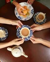 Top view of tea drink party woman hands pouring sharing teapot teacup saucer traditional biscuit Asian dress photo