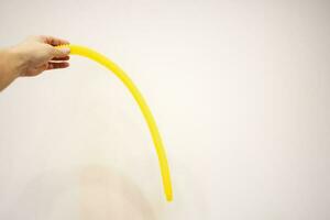 A man's hand holds a yellow rubber hose on a white background. impotence photo