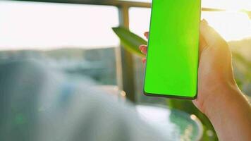 Woman sitting in a cafe and using smartphone with green mock-up screen in vertical mode. Girl browsing Internet video