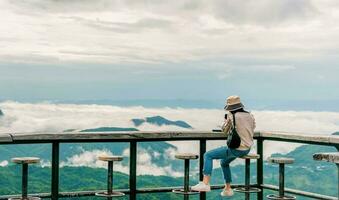 mujer sentado en de madera balcón mirando a montaña y niebla ver viaje foto