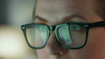 mujer en lentes mirando en el monitor y y trabajando con cartas y analítica. el monitor pantalla es reflejado en el lentes. video