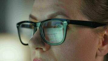 kvinna i glasögon ser på de övervaka och och arbetssätt med diagram och analyser. de övervaka skärm är reflekterad i de glasögon. video