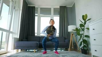 Frau Kniebeugen mit ein Katze im ihr Waffen, schleppend Bewegung. Zuhause Workouts video