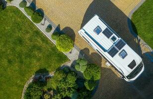Modern Camper Van with Solar Panels Installed Staying on Residential Driveway Aerial View photo