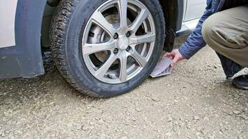 person placing wheel chock under wheel of civil vehicle tire to prevent its movement video
