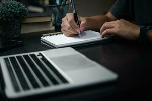 Man hand writing on notebook with computer laptop.Business planning, E learning , journal concept. photo